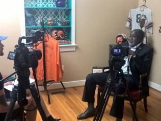Man in suit being filmed for interview, surrounded by cameras and Browns memorabilia.
