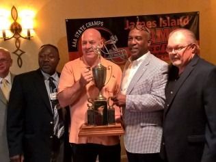 Men holding trophy; James Island All State Champs banner in background.