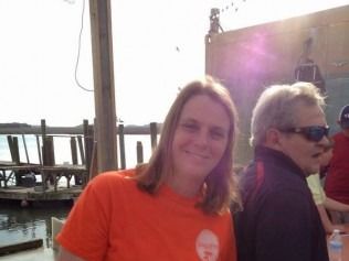 Woman in orange shirt smiling outdoors next to a man with sunglasses. 