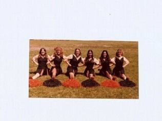 Six cheerleaders kneeling in grass, holding pom-poms. 