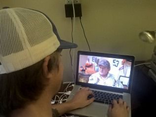 Person wearing a trucker hat watches a video on a laptop, hands on keyboard.