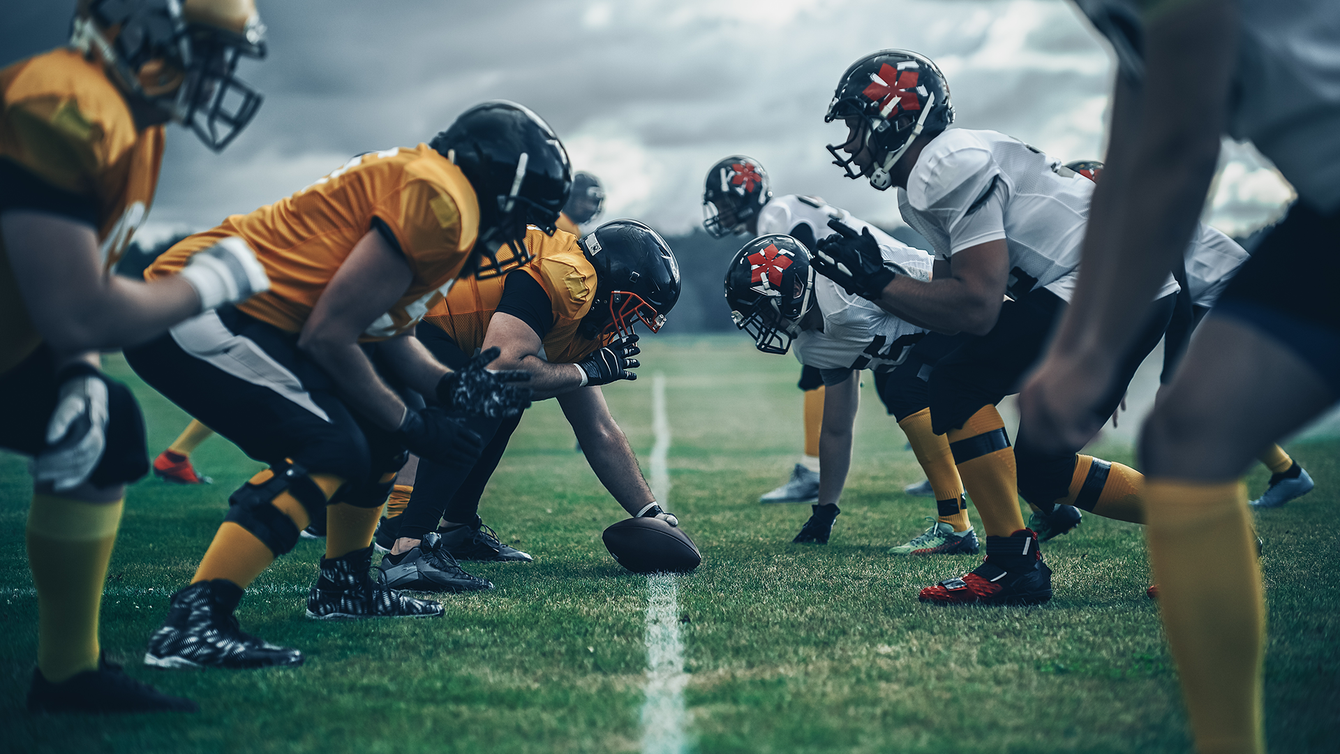Football teams line up facing each other on the field, ready for the play.