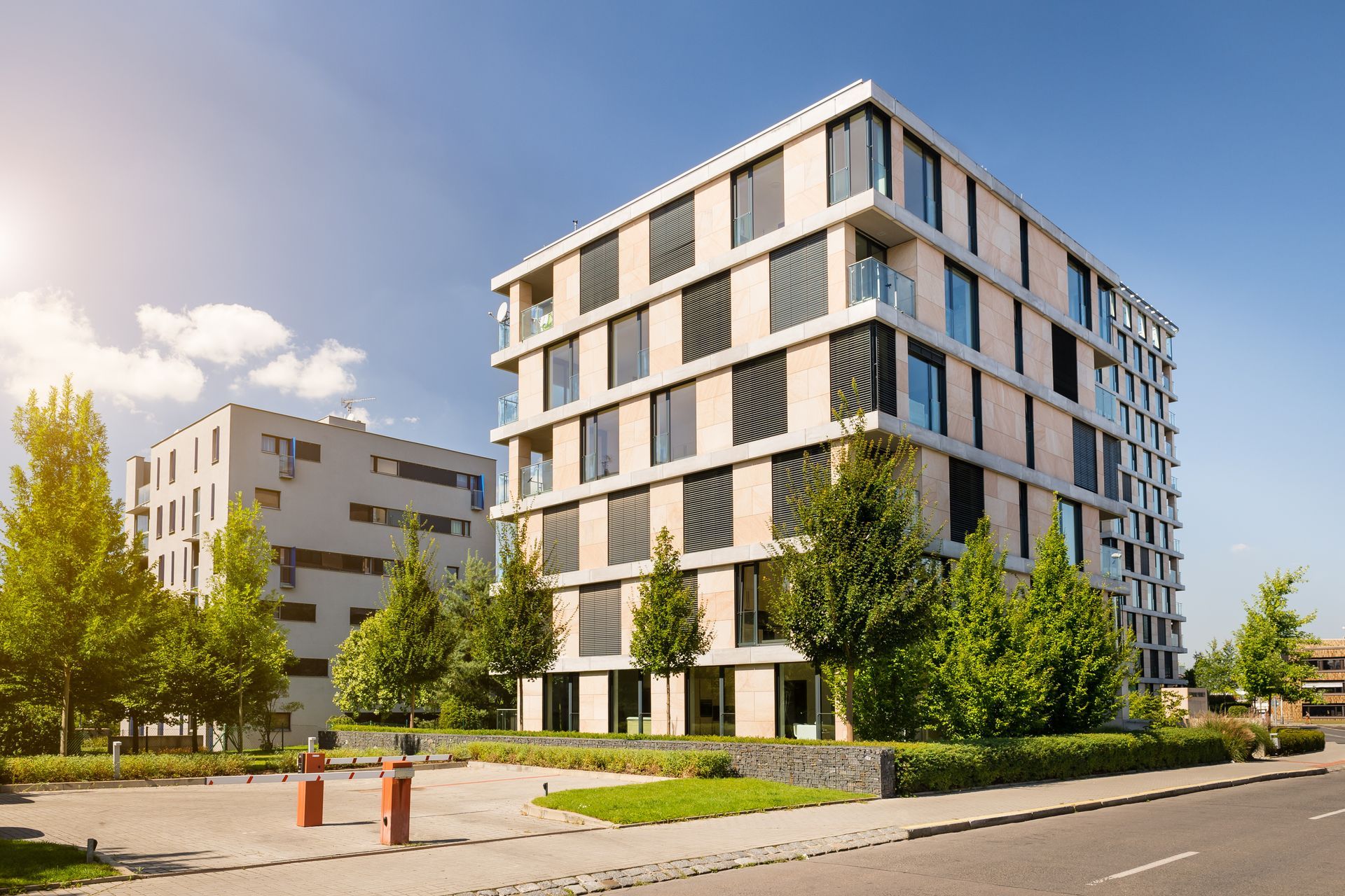 Modern multi-story apartment buildings with trees and a sunny sky.