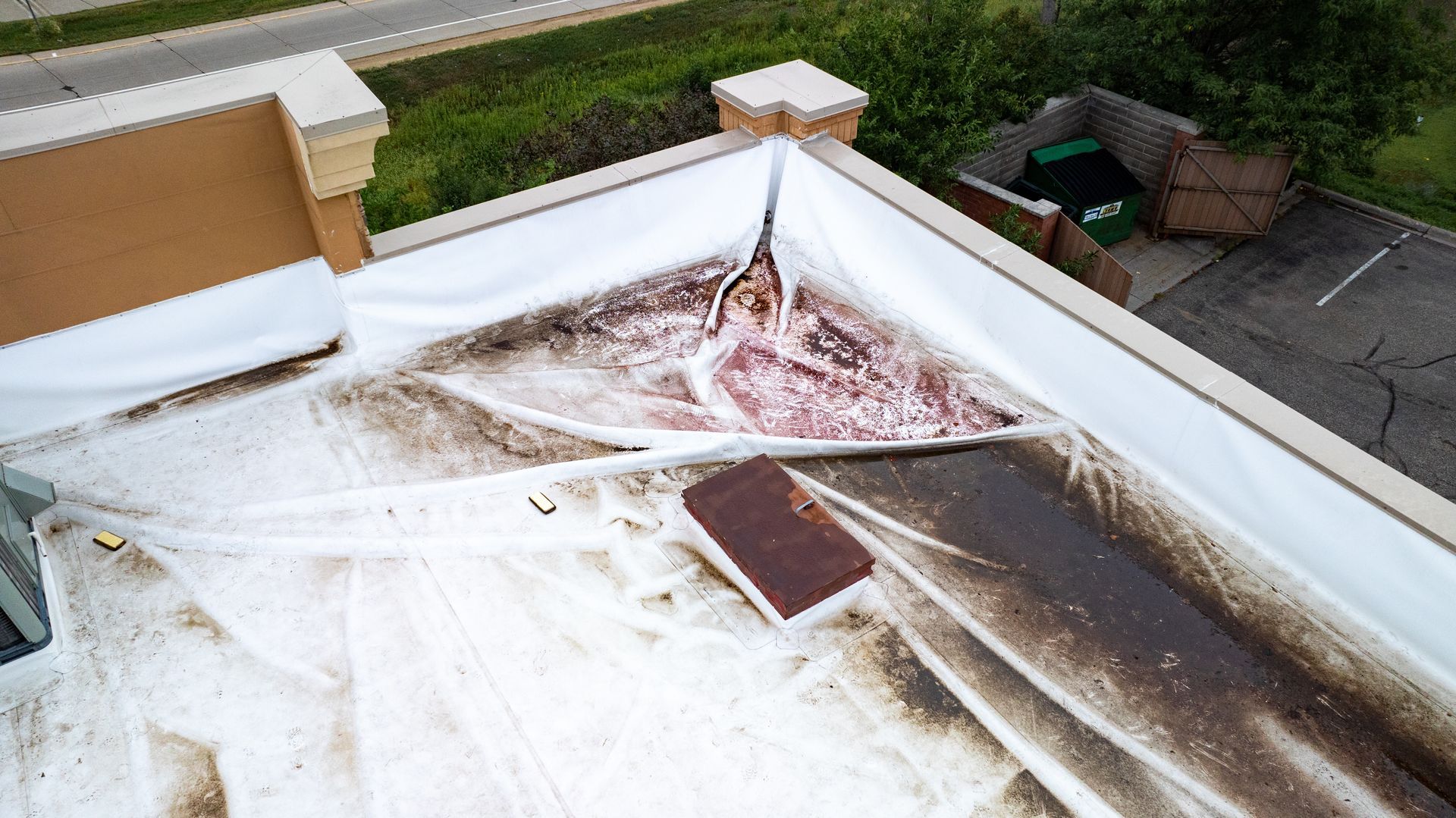 Damaged white commercial roof with brown stains, debris, and torn section.