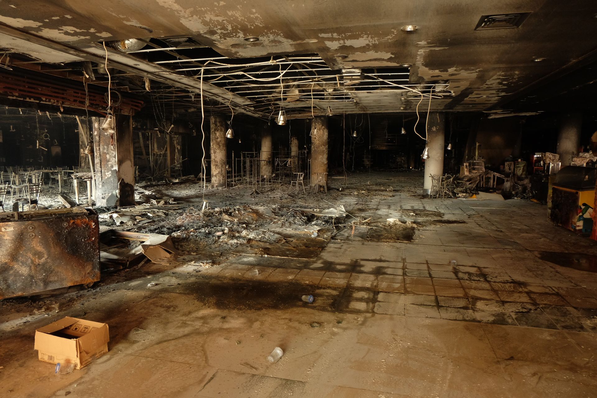 Interior view of a burned-out building with charred walls, debris on the floor, and exposed ceiling infrastructure.