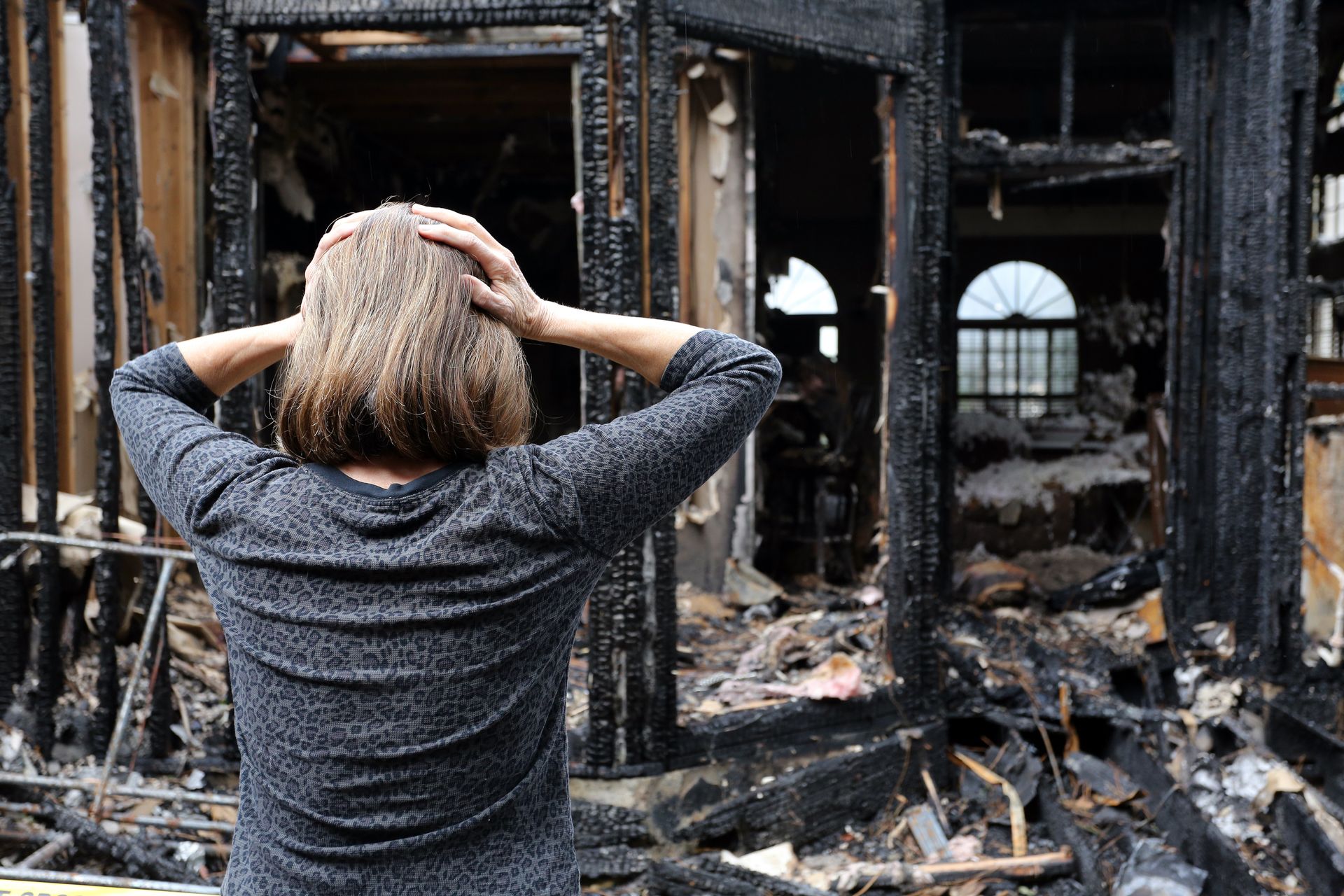 Woman with hands on head, looking at the charred remains of a building.