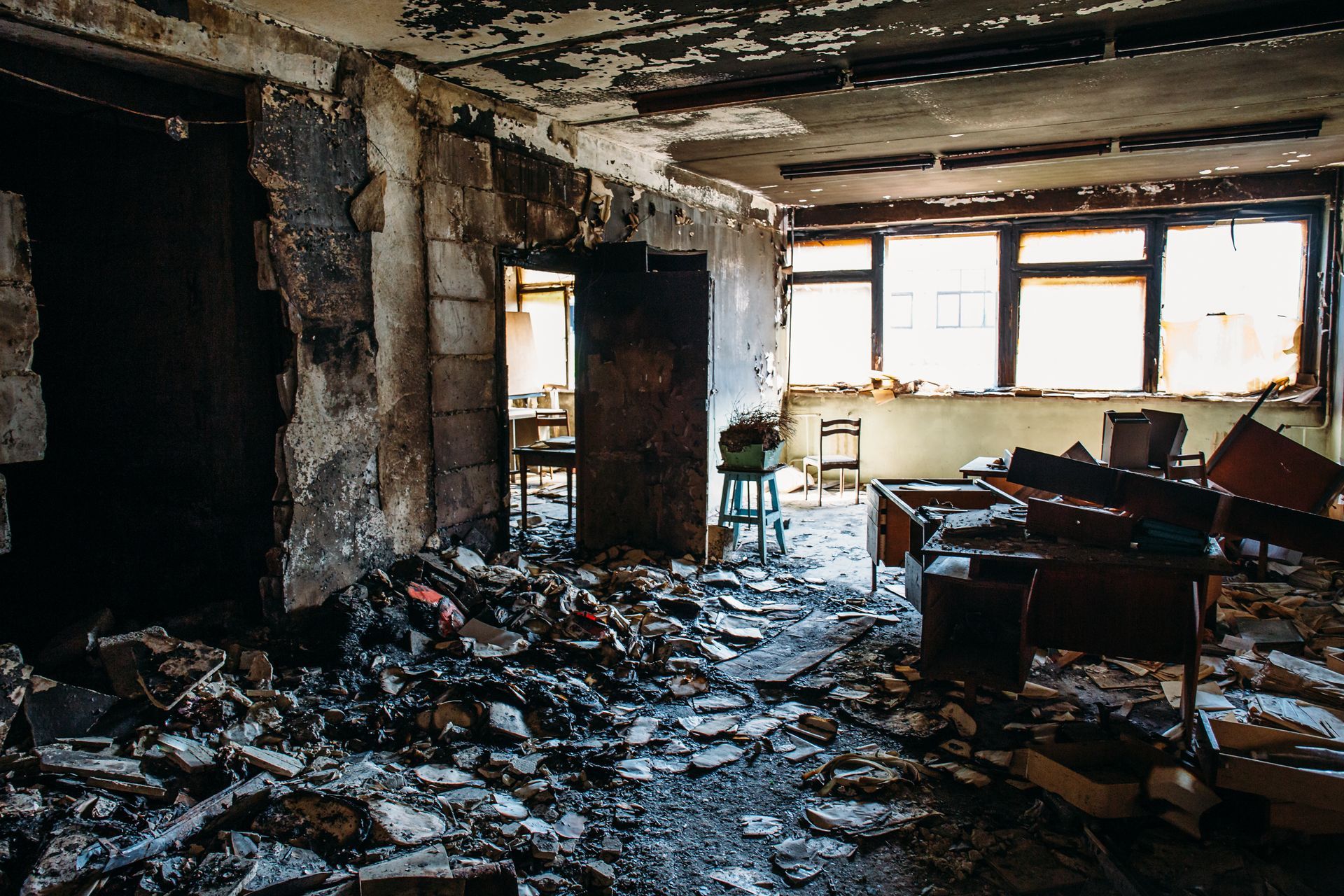Destroyed interior of a room, debris and rubble on the floor, damaged walls and windows.