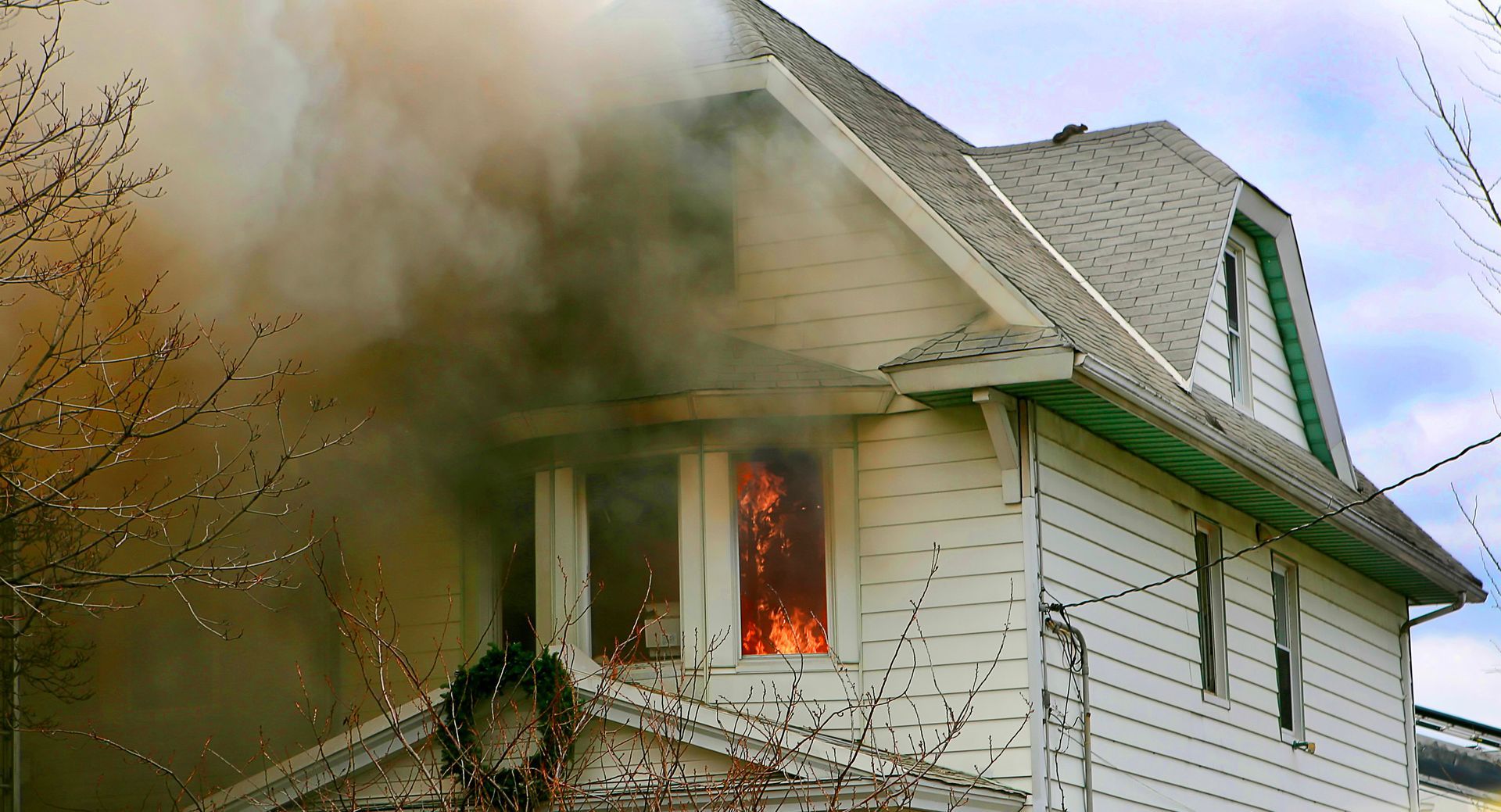 House on fire, flames visible through windows, smoke billowing, exterior shot.