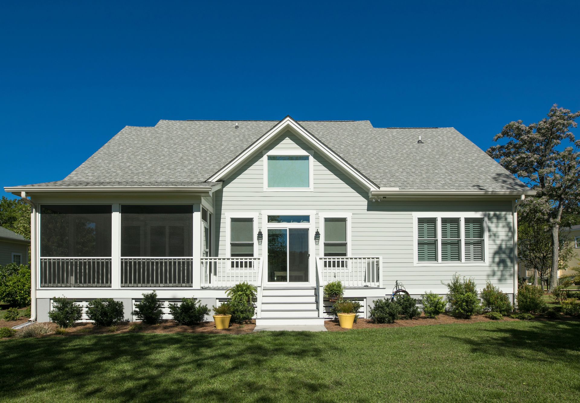 Light blue house with a screened porch, white trim, and a bright blue sky.