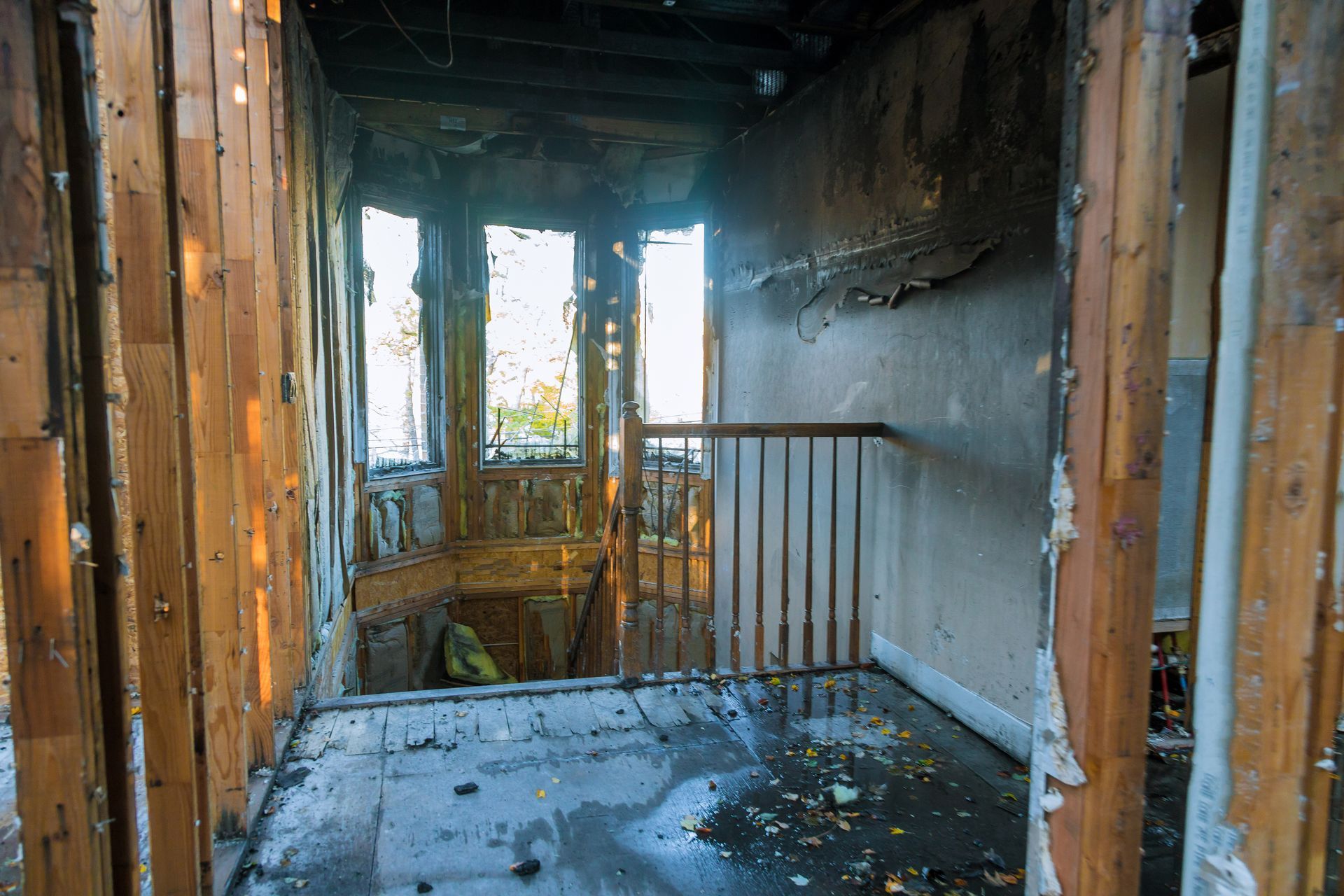 Interior of a fire-damaged building, showing burnt wood, stairwell, and debris.