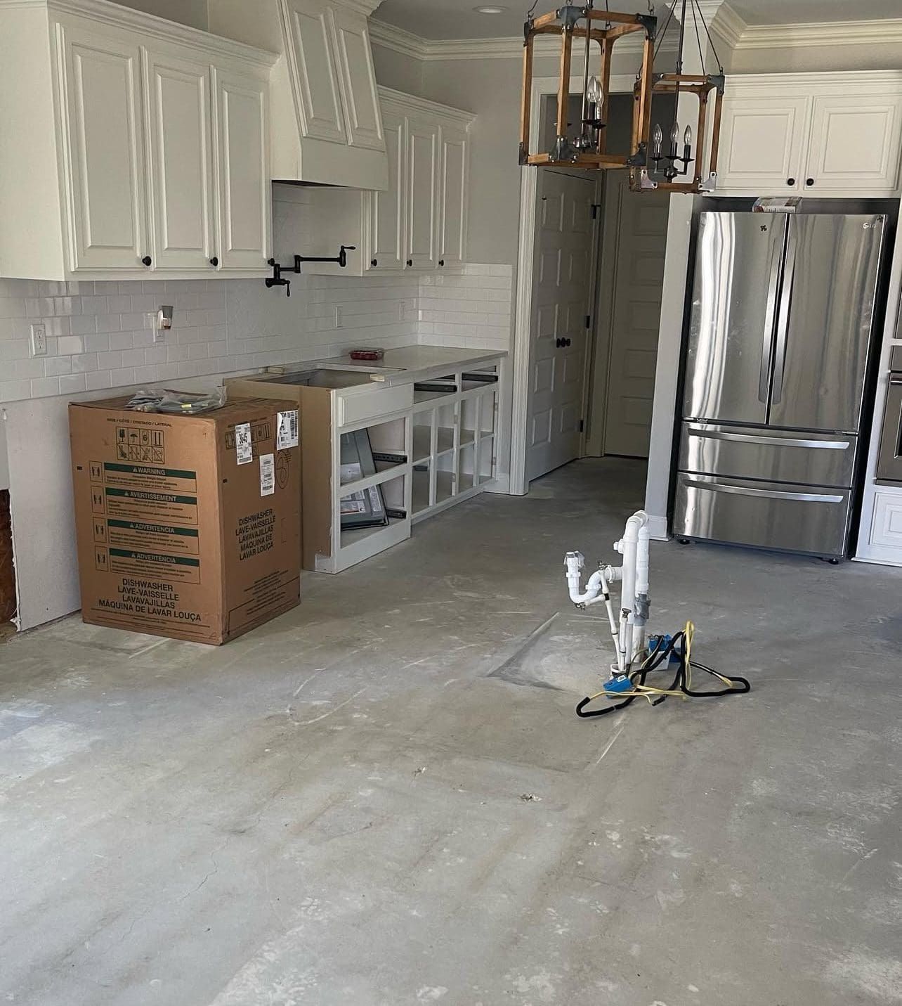 Kitchen under construction with white cabinets, stainless steel refrigerator, and a robotic floor cleaner.