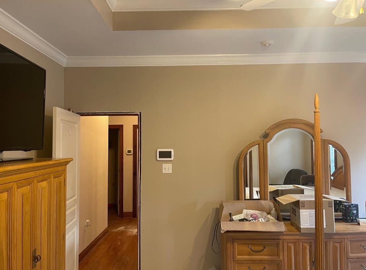 Bedroom with tan walls, white trim, wood furniture, and a doorway leading to a hallway.