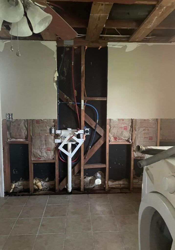Wall undergoing renovation, showing exposed framing, plumbing, insulation, and partially removed drywall.
