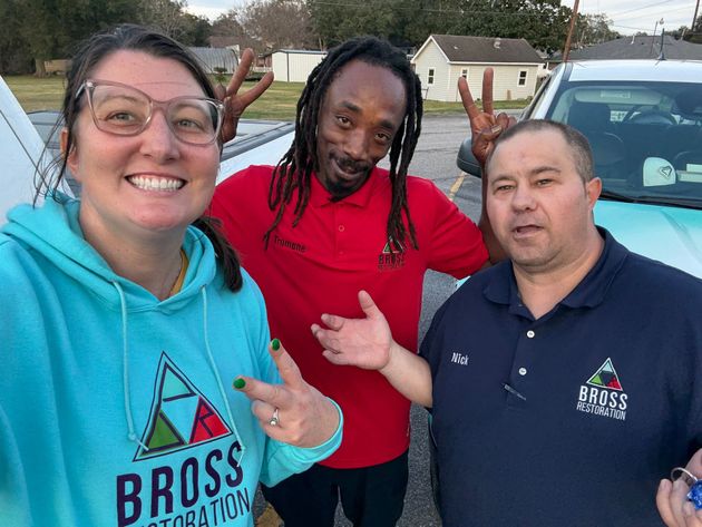 Three people smiling outdoors, one in a teal hoodie with BROSS Restoration logo, others in red and blue shirts; giving peace signs.
