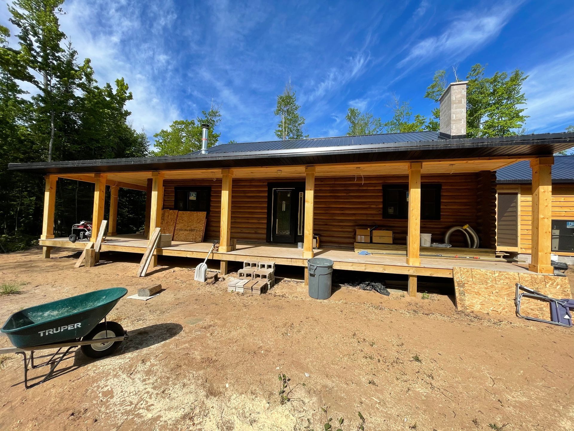 A green wheelbarrow is parked in front of a wooden house under construction.