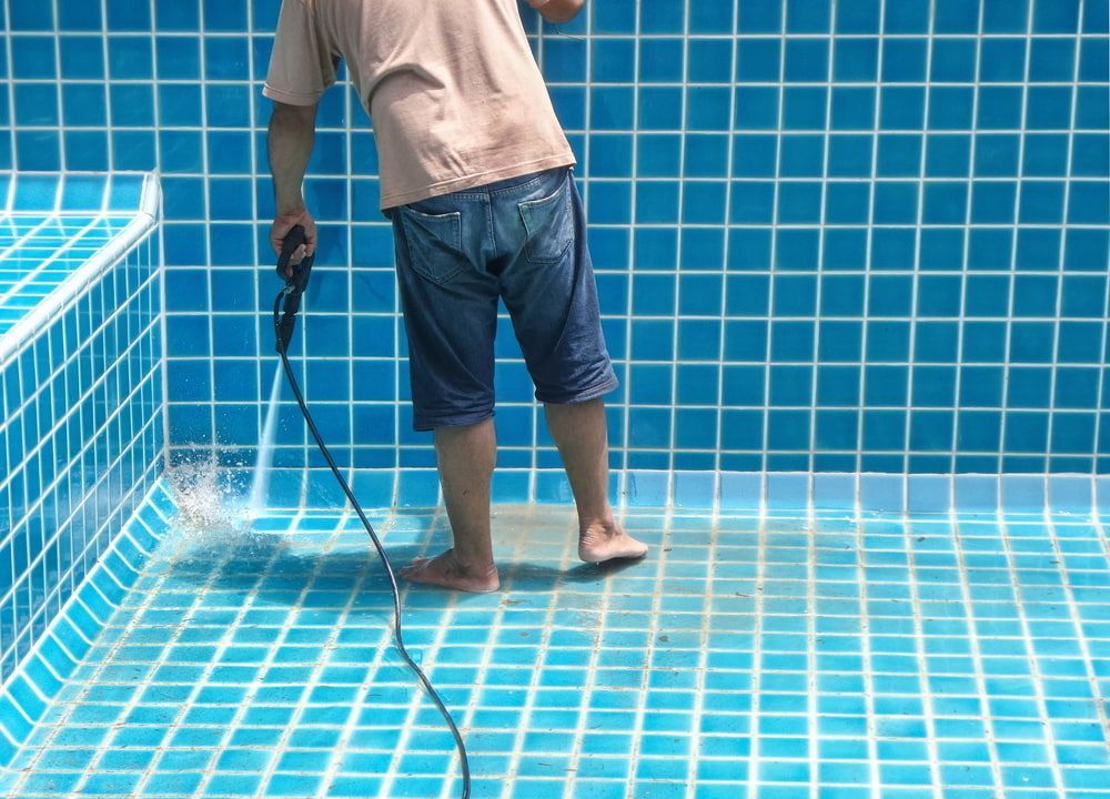Technician pressure cleaning an empty tiled swimming pool