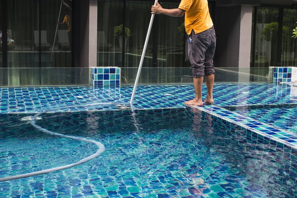 A Man Is Cleaning A Swimming Pool With A Vacuum Cleaner — Holiday Coast Pools & Water In Coffs Harbour, NSW
