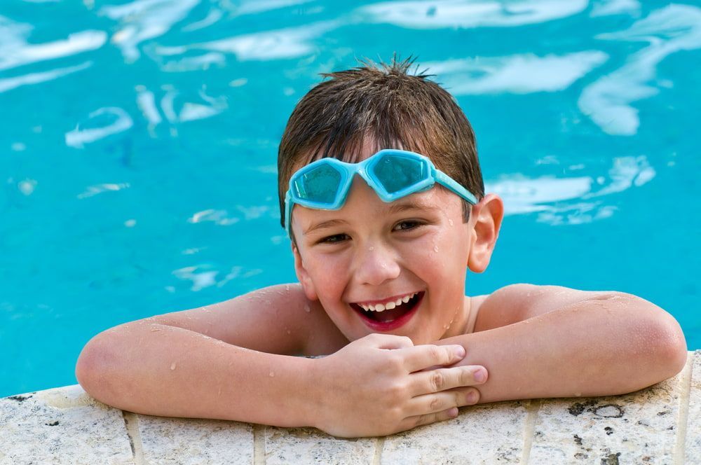A Young Boy Wearing Goggles Is Leaning On The Edge Of A Swimming Pool — Holiday Coast Pools & Water In Coffs Harbour, NSW