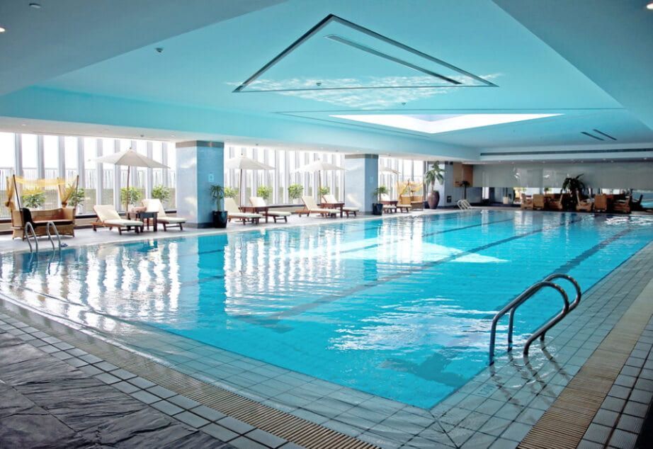 An Indoor Swimming Pool with Lounge Chairs and A View of The City Outside Large Windows — Holiday Coast Pools & Water In Coffs Harbour, NSW
