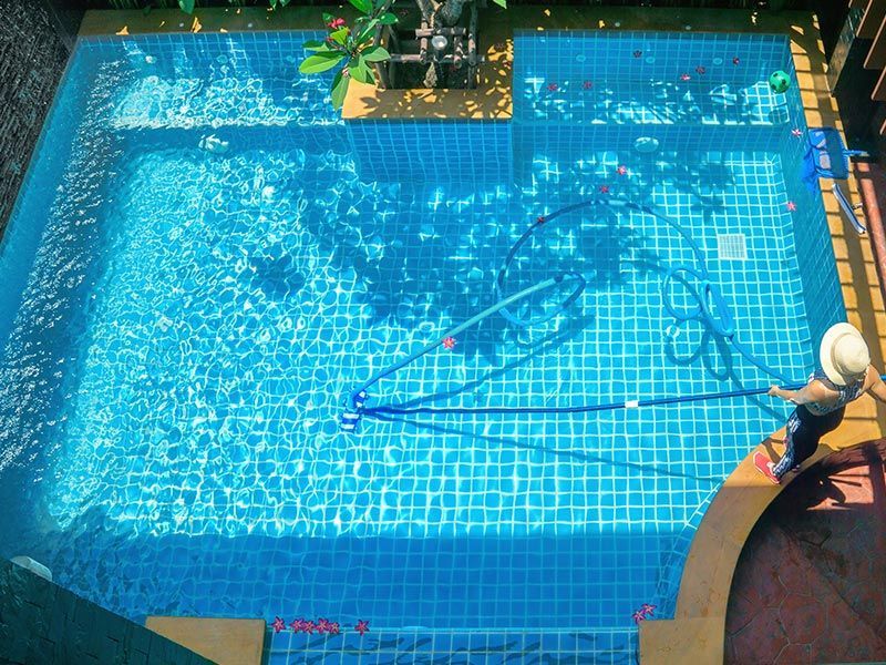 A Woman Is Cleaning A Swimming Pool With A Vacuum Cleaner — Holiday Coast Pools & Water In Coffs Harbour, NSW