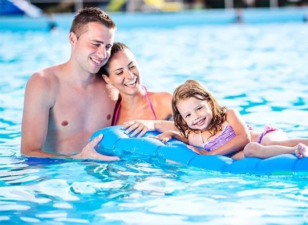A Man , Woman And Child Are Floating On A Blue Raft In A Swimming Pool — Holiday Coast Pools & Water In Coffs Harbour, NSW