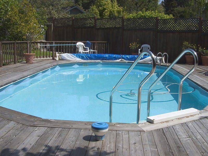 Swimming Pool Surrounded by A Wooden Deck, with A Blue Pool Cover and Ladder — Holiday Coast Pools & Water In Coffs Harbour, NSW