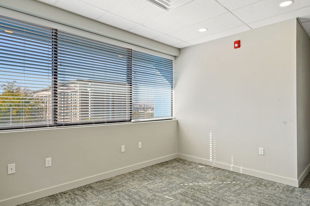 An empty room with a large window and blinds on the windows.