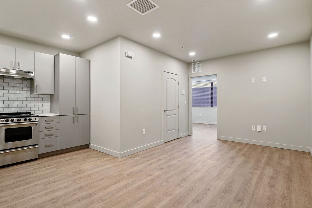 An empty living room with hardwood floors and a kitchen.