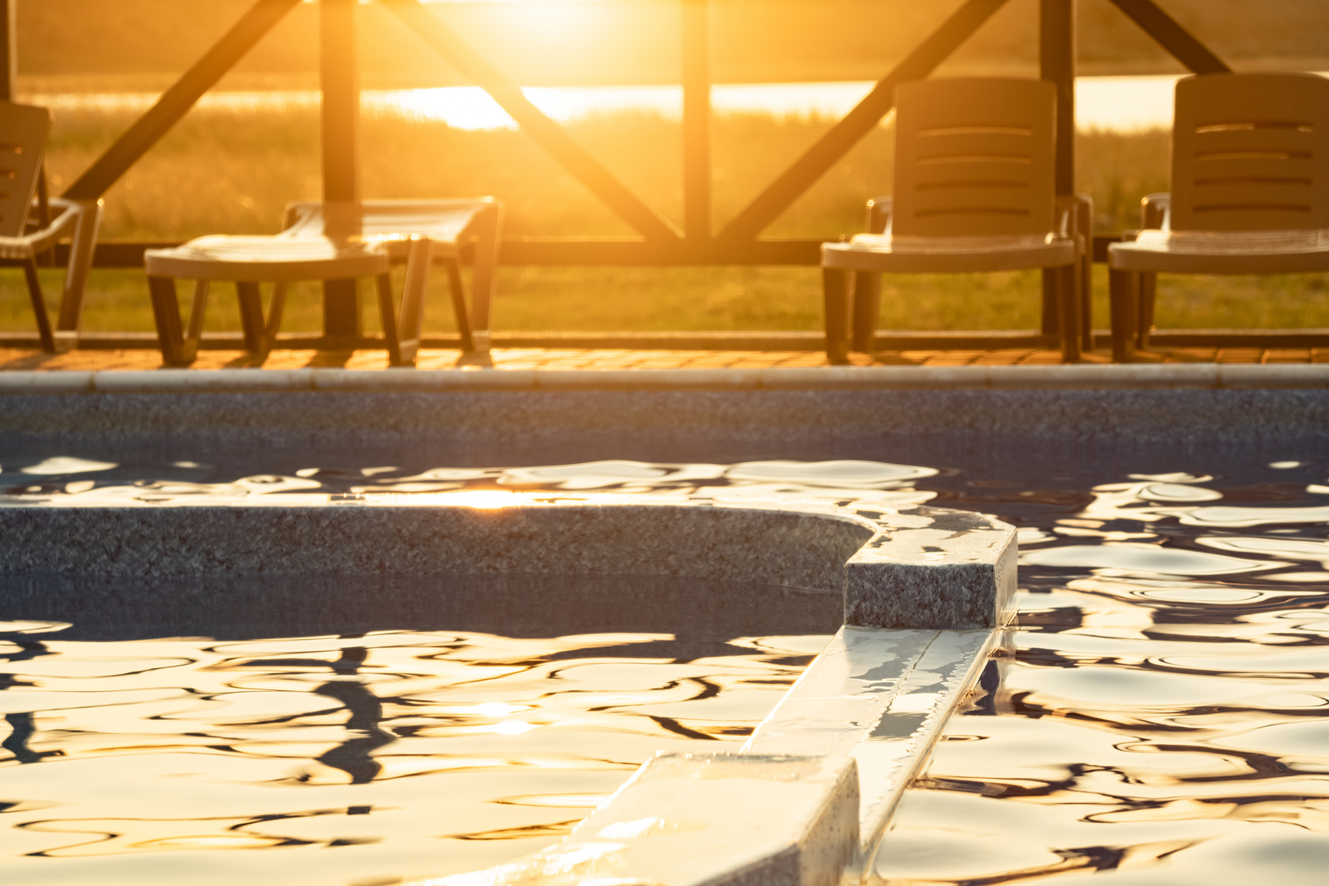 Sunlit swimming pool with rippling water and lounge chairs by a wooden deck at sunset
