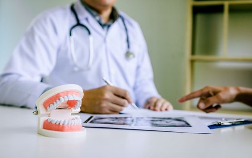 A doctor is sitting at a table with a model of teeth and talking to a patient.