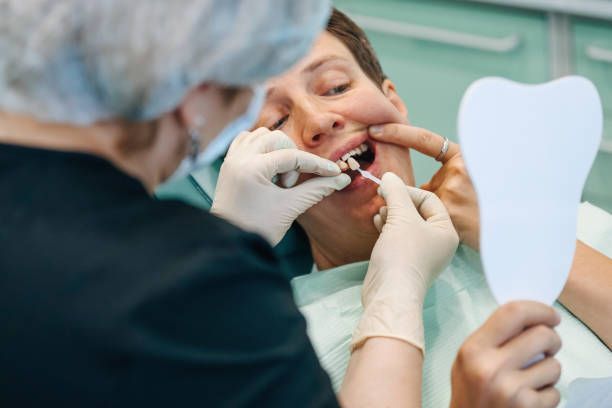 A man is sitting in a dental chair while a dentist is putting veneers.
