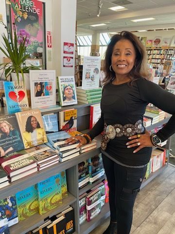 Diane is standing in a bookstore with her hands on her hips in front of her book Tragic Victory