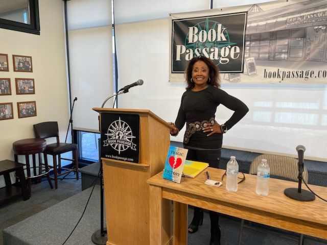Diane stands at a podium in front of a sign that says book passage