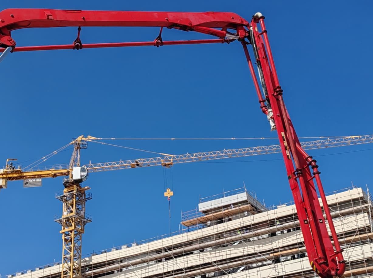 A Red Concrete Pump Is Being Used Into A Building Under Construction — Doug's Concrete Pumping Pty Ltd in Glenella, QLD