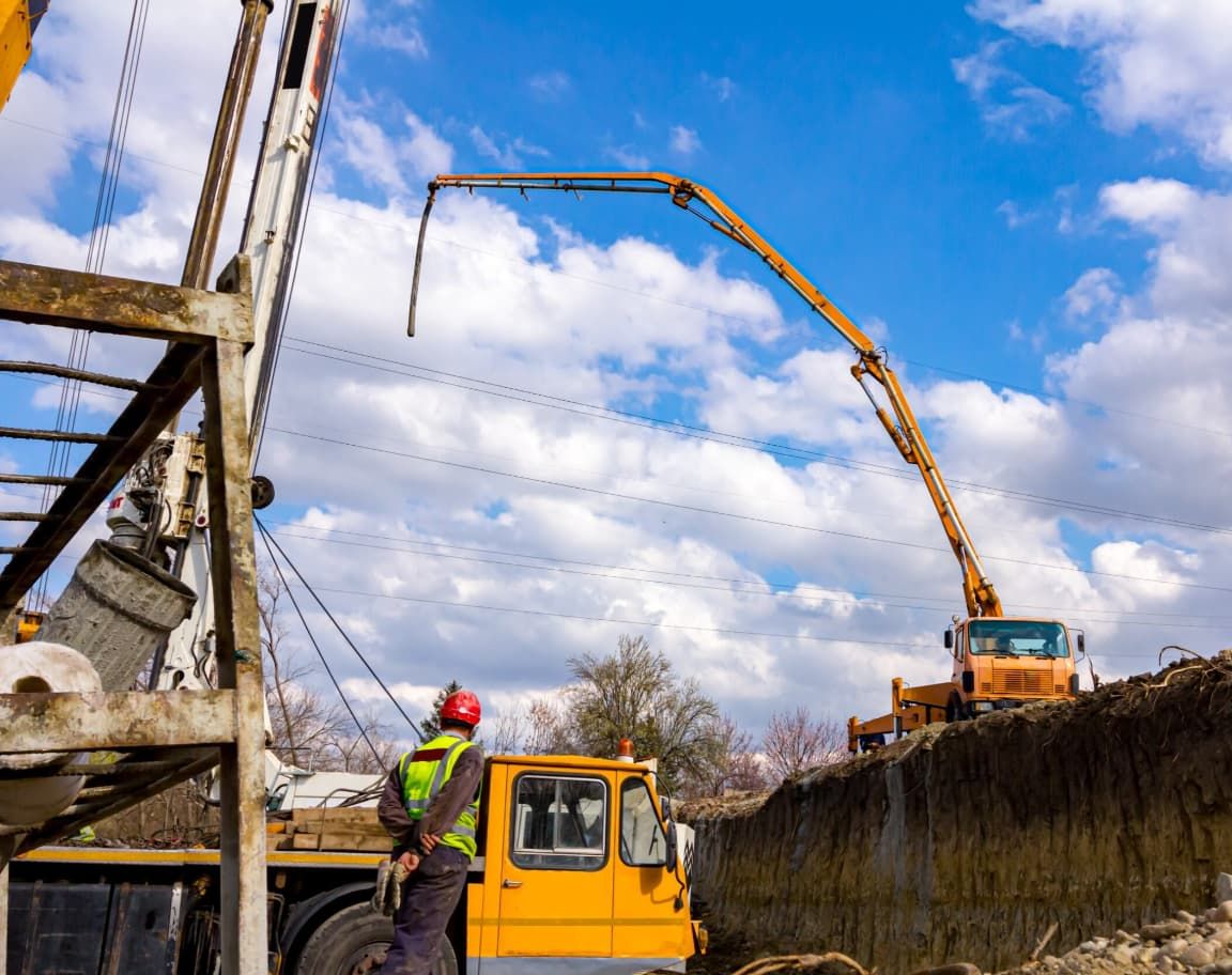 A Man Is Standing Next To A Yellow Truck With A Crane Attached To It — Doug's Concrete Pumping Pty Ltd in Glenella, QLD