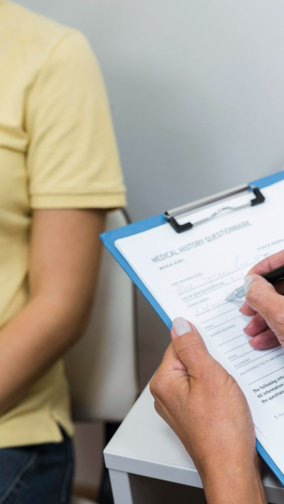 Doctor filling out a medical history form while seated next to a patient.