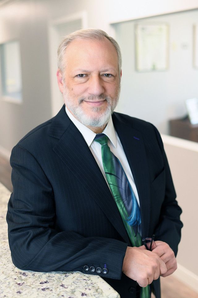 Man in suit with beard, green tie with blue design, smiles.