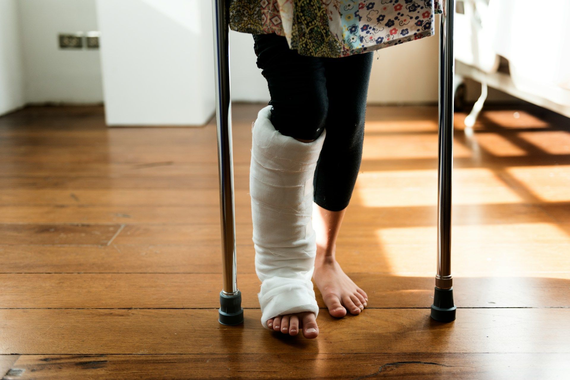 Person with a leg in a cast using crutches to walk on a wooden floor.