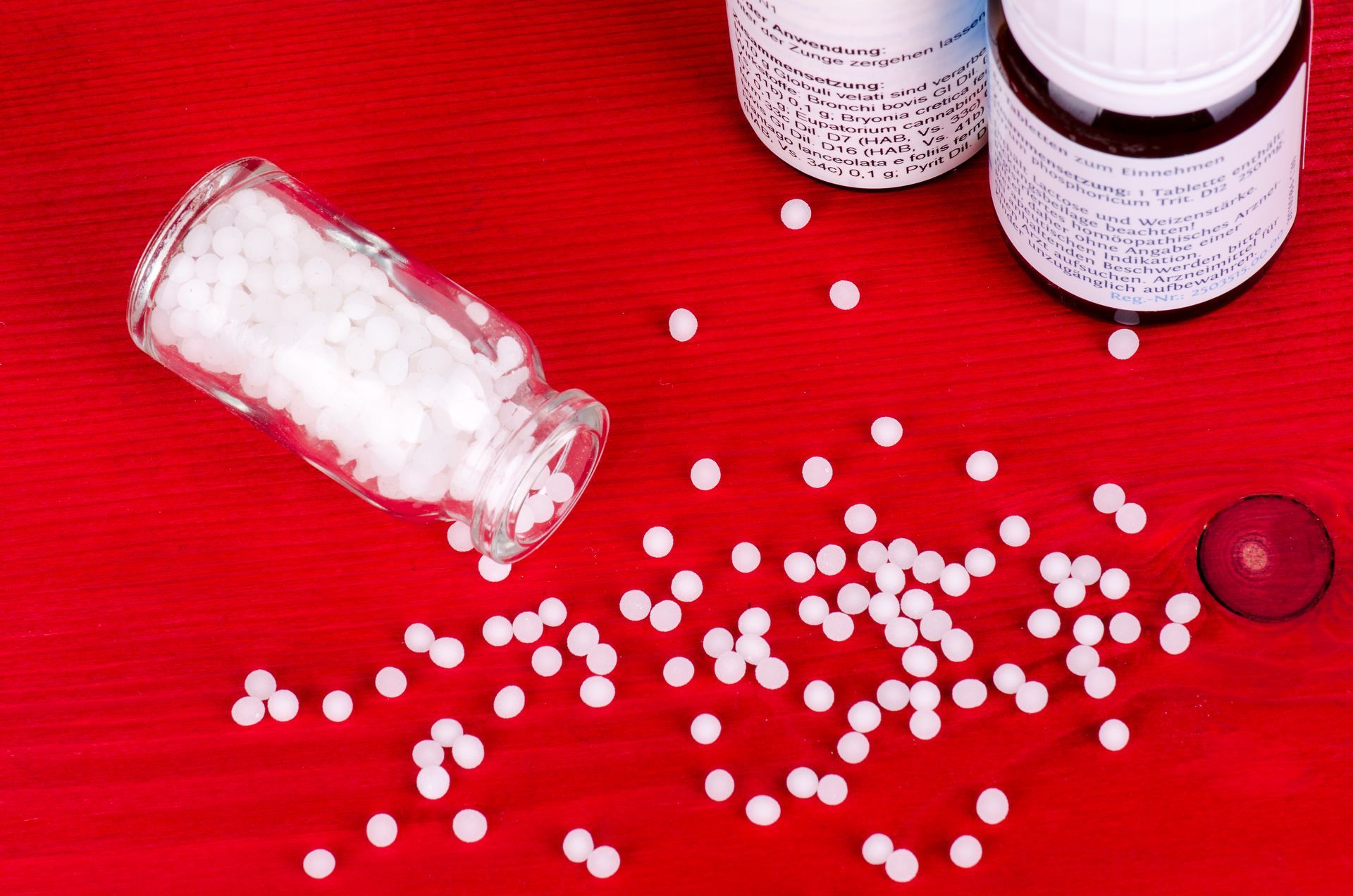 White pills spilled from a bottle onto a red surface, with two more bottles.