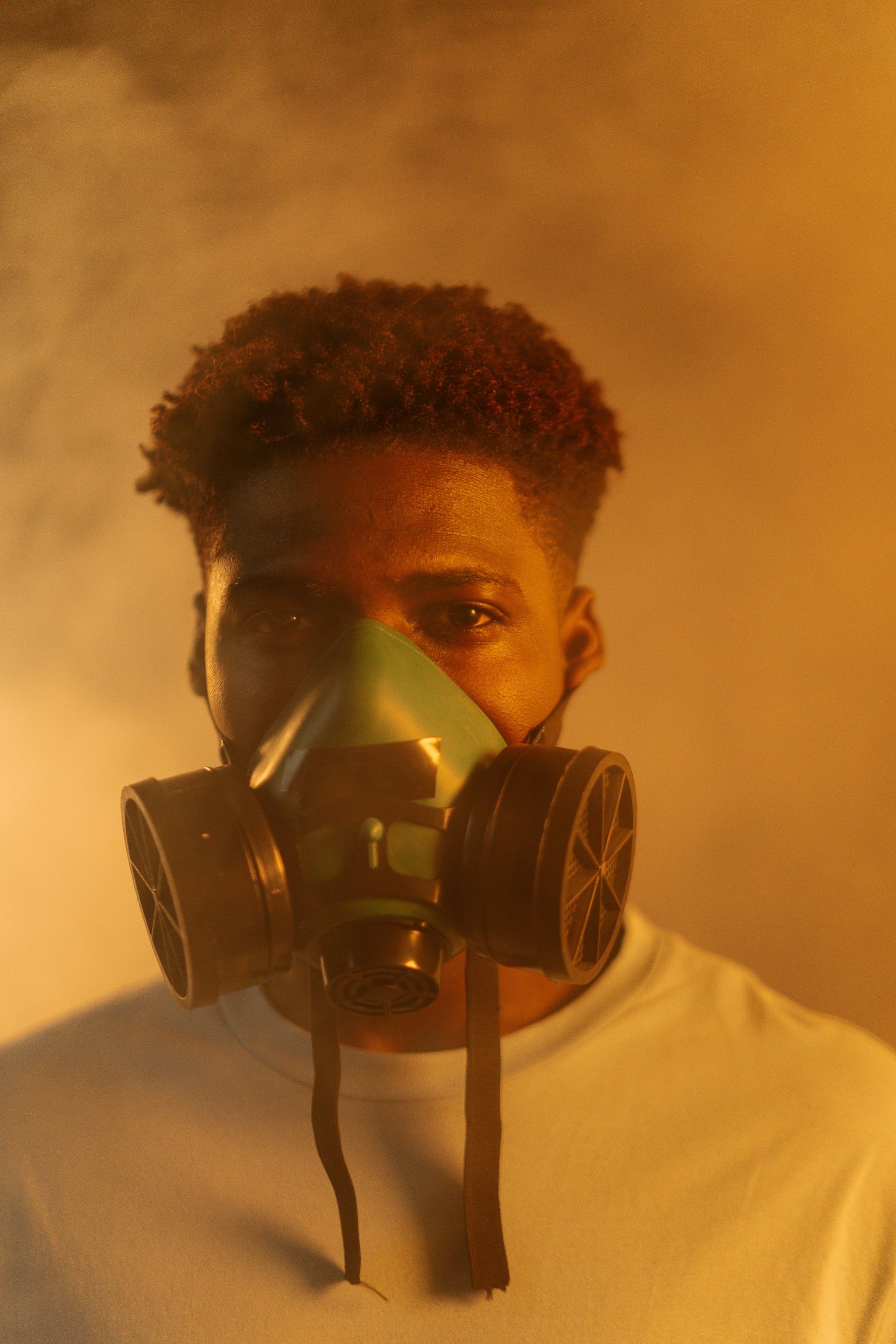 Man wearing a green gas mask in smoky, orange-lit environment.