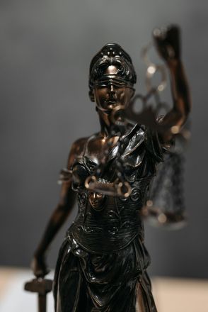 Statue of Lady Justice, blindfolded, holding scales and a sword, against a gray background.
