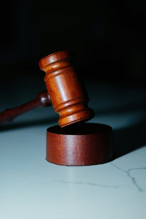 Wooden gavel on a circular stand, resting on a white surface, with a dark background.