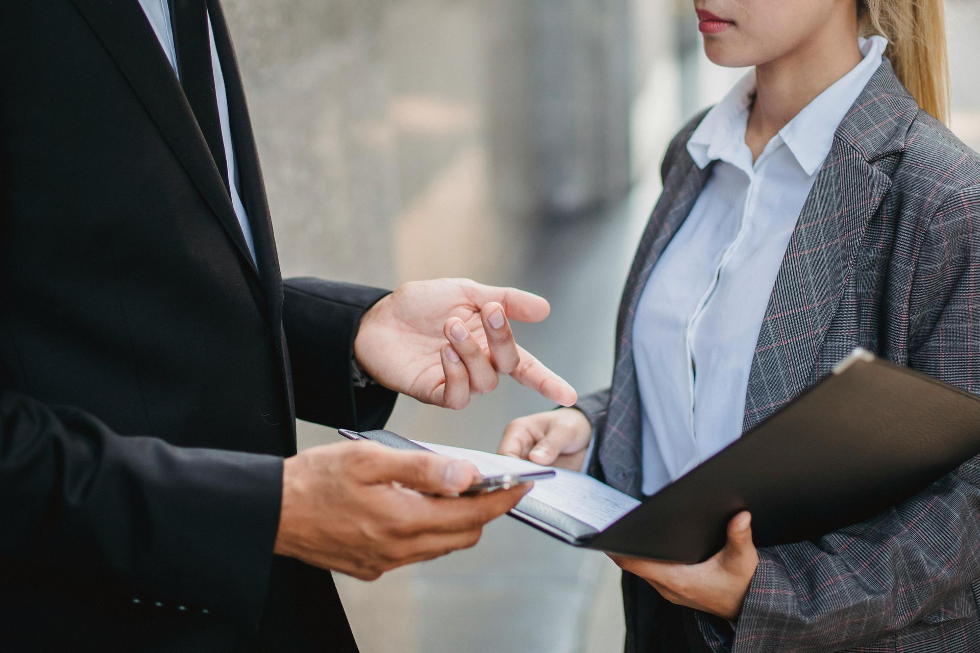 Two businesspeople exchanging a card during a meeting, with a laptop in view.