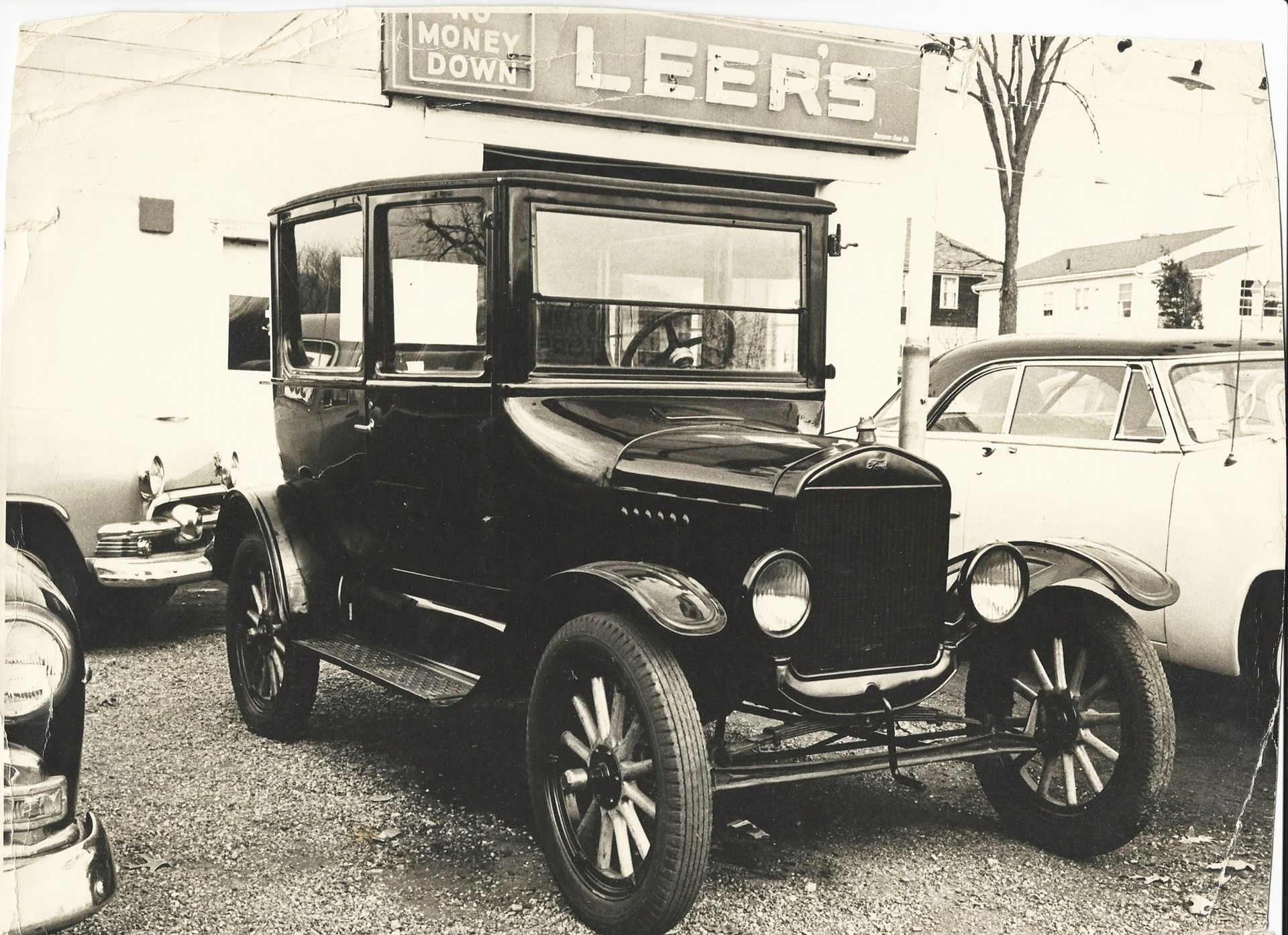 Black and white photo of a vintage Ford Model T parked in front of 