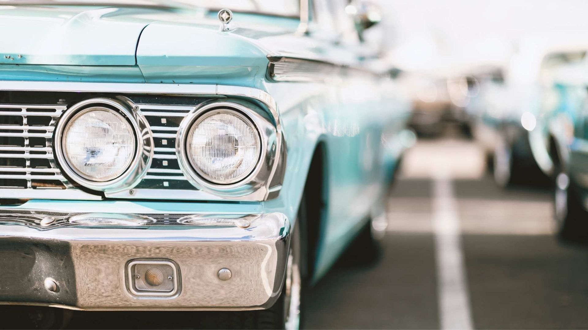 Classic light blue car with round headlights, parked in a lot.
