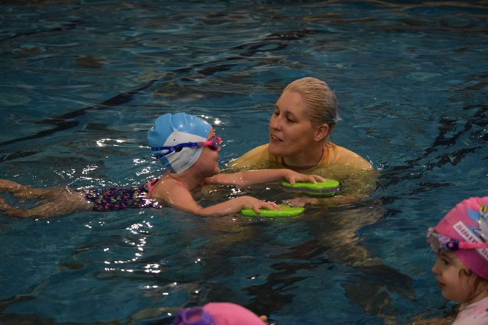 A Woman Is Teaching A Little Girl How To Swim In A Swimming Pool — Splash-A-Bout Swim School Pty Ltd In Mount Morgan, QLD