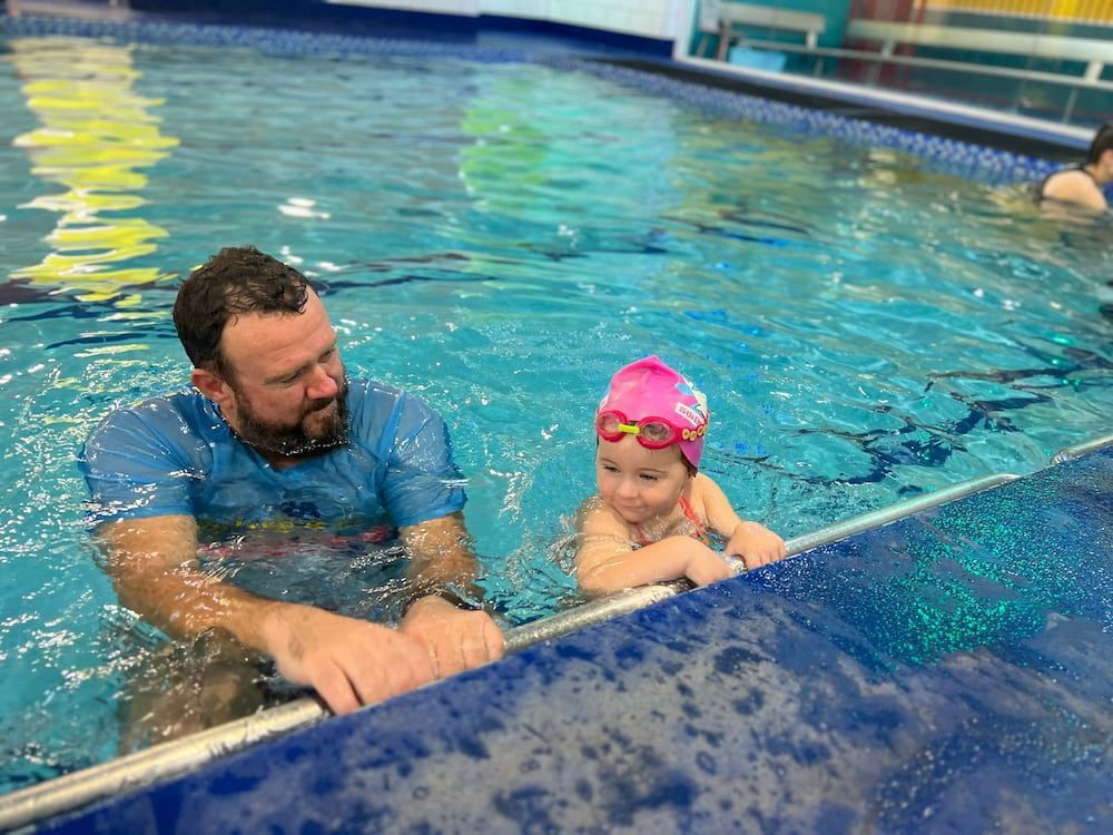 A Man Is Teaching A Little Girl How To Swim In A Swimming Pool — Splash-A-Bout Swim School Pty Ltd In Middlemount, QLD