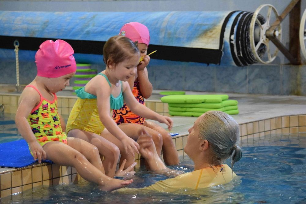 A Woman Is Assisting Toddlers Beside The Pool — Splash-A-Bout Swim School Pty Ltd In Biloela, QLD