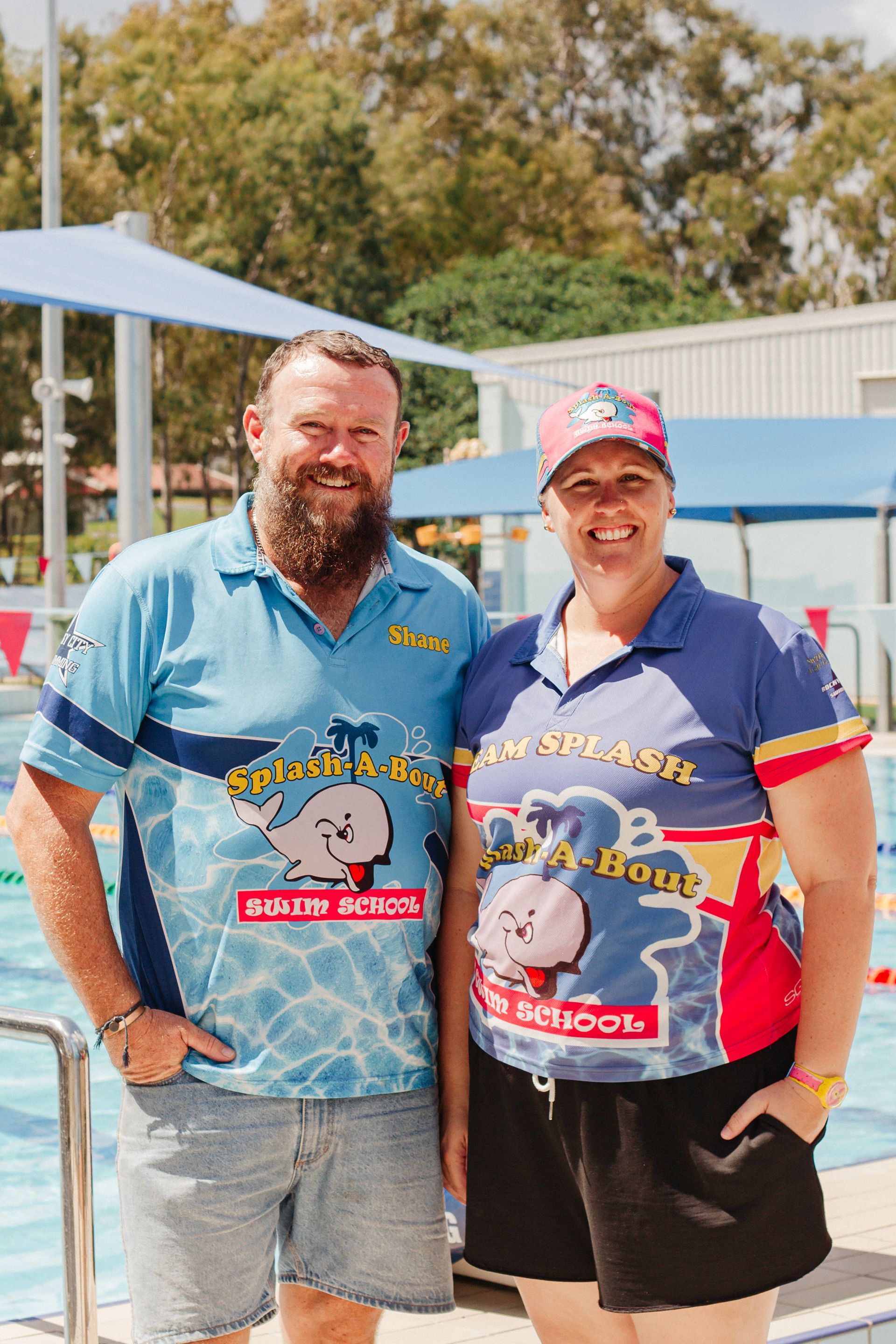 A Man And A Woman Are Standing Next To Each Other In Front Of A Swimming Pool — Splash-A-Bout Swim School Pty Ltd In Park Avenue, QLD
