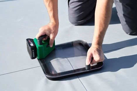 A person is using a green tool to cut a piece of plastic.